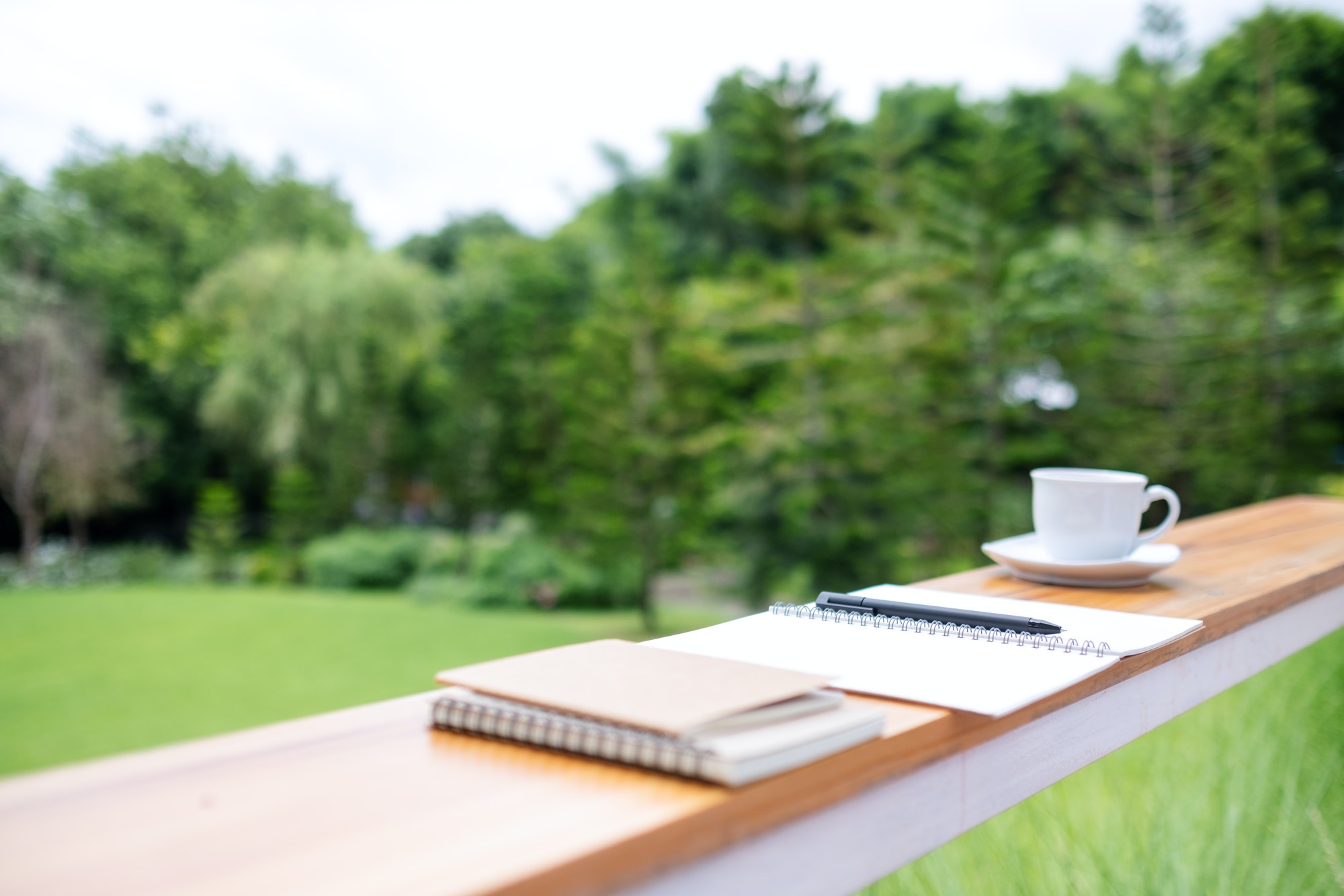 Book, notebooks and coffee cup on wooden table in the outdoors